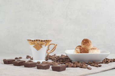 Çikolatalı fincan, kasede hamur işleri ve masada kahve çekirdekleri.