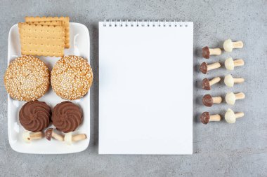 Not defterinin yanında bir tabak kurabiye ve mermer arka planda çikolatalı mantar. Yüksek kalite fotoğraf