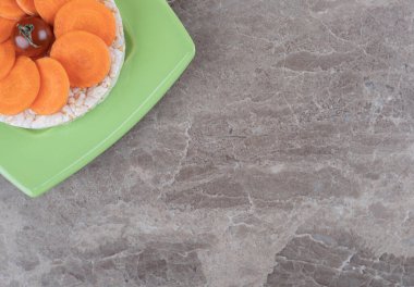 Havuç dilimlerinin ortasında kırmızı domates ve mermer zemin üzerinde, tabağın altında pirinç keki. Yüksek kalite fotoğraf