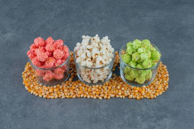 Mermer zemin üzerinde mısır taneleriyle çevrili küçük kaseler dolusu patlamış mısır. Yüksek kalite fotoğraf