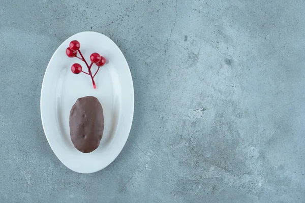 Small chocolate coated cake and a cluster of christmas berries on a platter on marble background. High quality photo