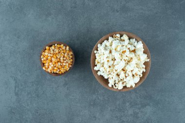 İki küçük kase dolusu tuzlu patlamış mısır ve mermer zemin üzerinde taze mısır taneleri. Yüksek kalite fotoğraf