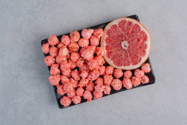 Bir tabak kırmızı patlamış mısır şekeri ve mermer arka planda bir dilim greyfurt. Yüksek kalite fotoğraf