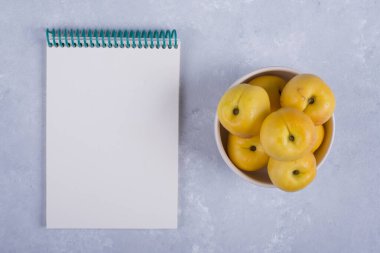 Beyaz bir seramik kasede, yanında defter olan sarı şeftaliler. Yüksek kalite fotoğraf