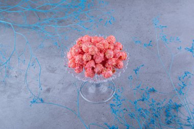 Cam şeker tutacağı patlamış mısır şekeriyle dolu mermer arka planda dekoratif mavi dalların yanında. Yüksek kalite fotoğraf