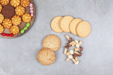 Tahta tahtada, mermer zemin üzerinde şekerlemelerle çevrili çeşitli kurabiyelerin yanında küçük kurabiye ve çikolata mantarları yığını. Yüksek kalite fotoğraf