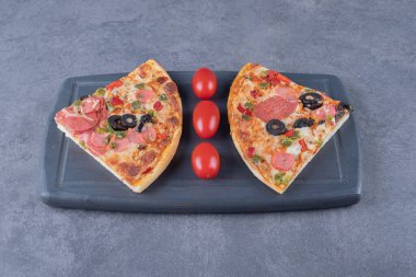 Gri tahta üzerinde domatesli iki pepperoni pizza dilimi. Yüksek kalite fotoğraf