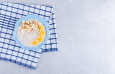 Havlunun üzerinde bir kase lezzetli yulaf ezmesi, üzerinde doğranmış elma ve portakal parçaları mermer arka planda. Yüksek kalite fotoğraf