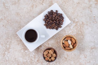 Kahve çekirdeğinin yanında küçük atıştırmalıklar ve mermer arka planda bir fincan kahve. Yüksek kalite fotoğraf