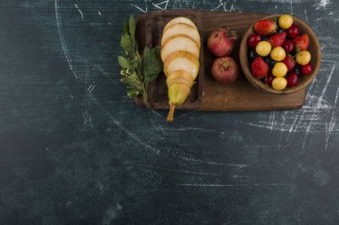 Kesilmiş armut ve meyveler koyu mermer arka planda izole edilmiş.