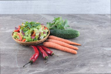 Fesleğen yaprağı, salatalık, havuç ve biber mermer arka planda bir kase salatanın yanında. Yüksek kalite fotoğraf