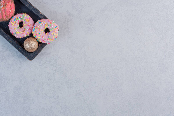 Delicious donuts with sprinklers and Christmas ball on black plate. High quality photo