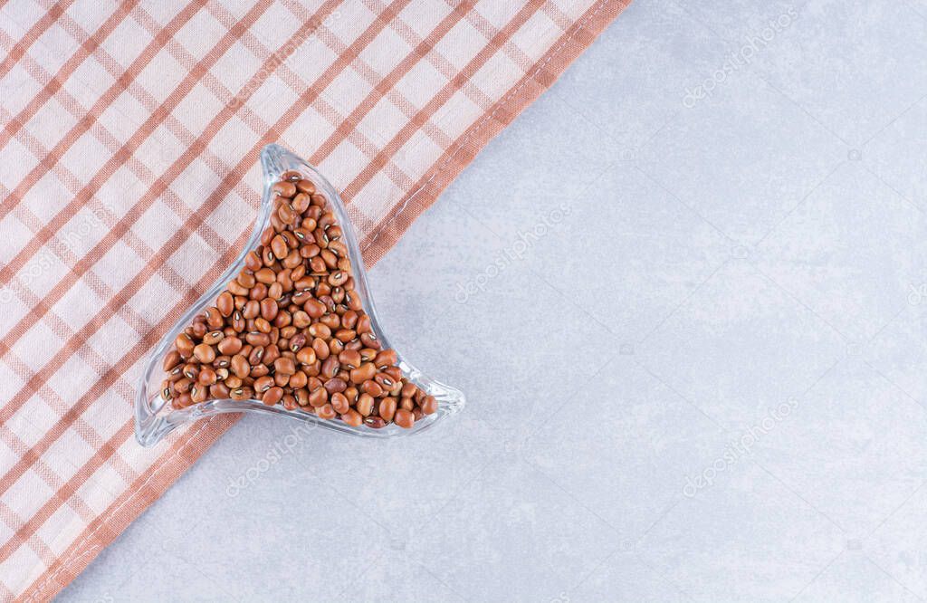 Ornate trinagular plate full of red beans on tablecloth, on marble background. High quality photo