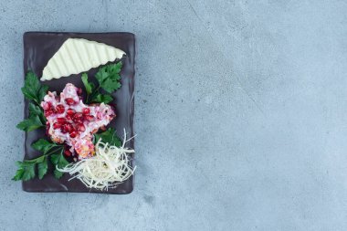 Peynirle süslenmiş salata porsiyonu, maydanoz yaprakları ve mermer zemin üzerinde siyah bir tabakta nar. Yüksek kalite fotoğraf