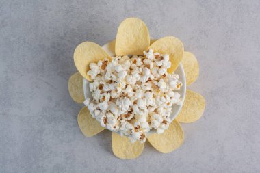 Patates cipsi mermer arka planda bir tabak patlamış mısırın etrafını sarıyor. Yüksek kalite fotoğraf