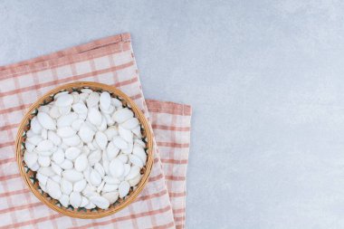 Örülmüş bir sepetin altında katlanmış masa örtüsü mermer zemin üzerinde beyaz kabak tohumlarıyla dolu. Yüksek kalite fotoğraf