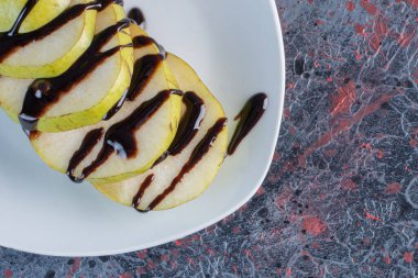 Dilimlenmiş elmanın beyaz tabakta çikolatayla yakın fotoğrafını çek. Yüksek kalite fotoğraf