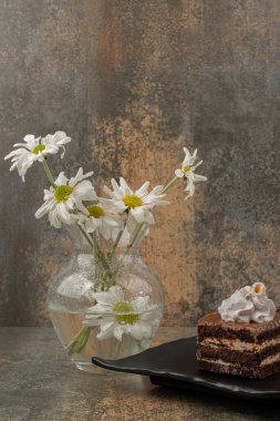 Bir buket papatya çayı ve siyah tabakta bir parça çikolatalı kek. 