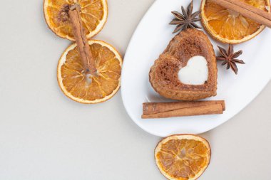 Kalp şeklinde pasta, portakal dilimleri, karanfil ve tarçınlı beyaz tabak. Yüksek kalite fotoğraf