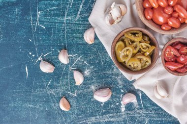 Mavi arka planda sarımsak ve masa örtüsüyle turşulu domates ve jalapeno kaseleri. Yüksek kalite fotoğraf