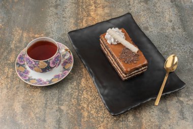 Koyu tabakta sıcak çay ve kaşık olan bir parça kek. 