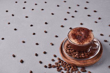 Gri arkaplanda kahve çekirdekleri olan bir fincan kahve.