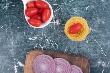 Çiğ, yuvarlak makarna, soğan dilimleri ve tahta tahtada beyaz bir tabak küçük domates. Yüksek kalite fotoğraf