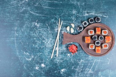Klasik suşi çeşitleri ahşap tahtanın üzerinde çubuklarla yuvarlanıyor. Yüksek kalite fotoğraf
