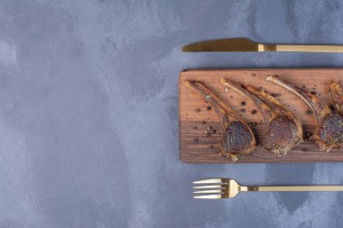 Ahşap tahtada kuzu pirzolası ve mavi arka planda çatal bıçak takımı. Yüksek kalite fotoğraf