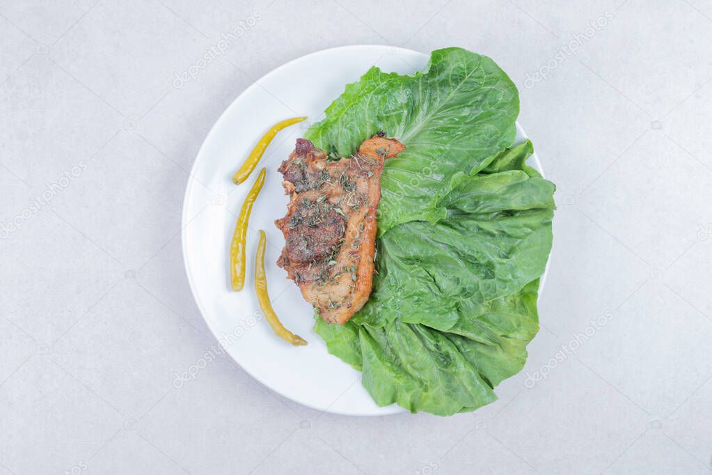 Grilled lamb chop on white plate with pickled pepper and lettuce. High quality photo