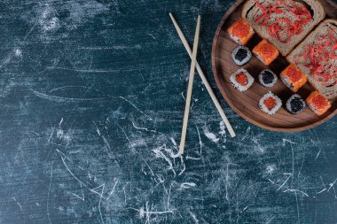 Çeşitli suşi ruloları, ekmek dilimleri ve ahşap tabakta çubuklar. Yüksek kalite fotoğraf