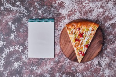 Ahşap bir tahtanın üzerinde bir dilim pizza ve bir yemek tarifi kitabı. Yüksek kalite fotoğraf