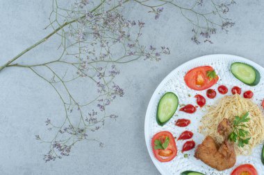 Beyaz tabakta sebze salatası, makarna ve mermer arka planda tavuk.