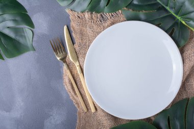 Beyaz plaka etrafında yapay yeşil yapraklar ve mavi arka planda çatal bıçak takımı. Yüksek kalite fotoğraf