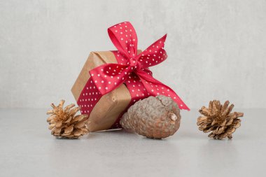 Kırmızı fiyonklu küçük bir hediye kutusu ve beyaz arka planda bir sürü kozalak.