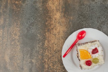 Beyaz tabakta kırmızı kaşık olan bir dilim tatlı pasta.