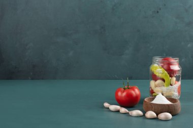 Cam kavanozda turşu, taze sarımsak, domates ve mavi arka planda tuz kasesi. Yüksek kalite fotoğraf