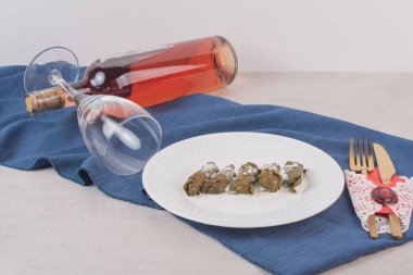 Beyaz arka planda üzüm yaprağı dolma, gül şarabı şişesi ve çatal bıçak takımı. Yüksek kalite fotoğraf
