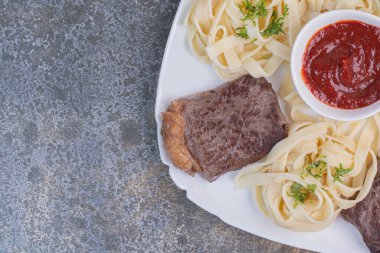 Yeşillikli makarna ve domates ezmesi, beyaz tabakta et.