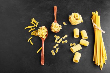 Tahta kaşıkta ve siyah arka planda çiğ makarna çeşitleri. Yüksek kalite fotoğraf