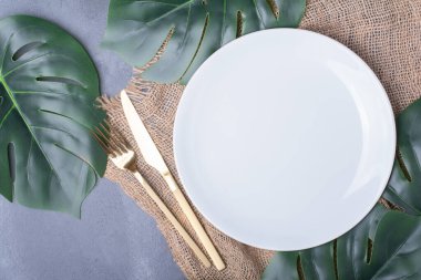 Beyaz plaka etrafında yapay yeşil yapraklar ve mavi arka planda çatal bıçak takımı. Yüksek kalite fotoğraf