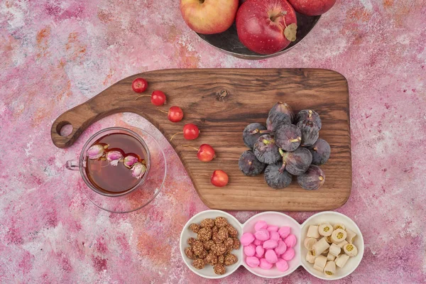 Purple figs on a wooden board with tea and candies around. High quality photo