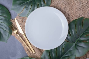 Beyaz plaka etrafında yapay yeşil yapraklar ve mavi arka planda çatal bıçak takımı. Yüksek kalite fotoğraf