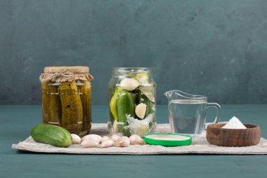 Cam kavanozda sebze turşusu ve mavi zemin üzerinde salatalık ve sarımsaklı tuz kasesi. Yüksek kalite fotoğraf