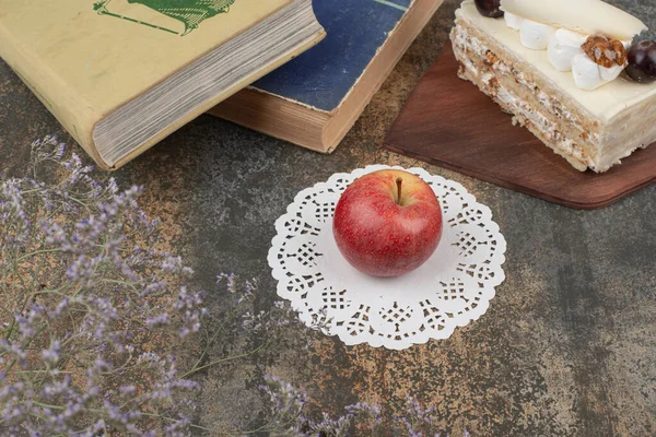 Red apple with books and piece of cake on marble background