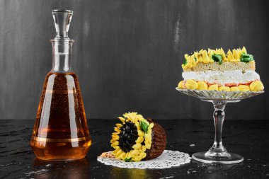 Siyah arka planda bir şişe içkiyle birlikte ayçiçeği şeklinde bir pasta. Yüksek kalite fotoğraf