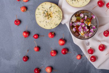 Yarısı kesilmiş meyve, kiraz ve limon dilimli bir bardak meyve suyu ve mavi arka planda masa örtülü çiçekler.