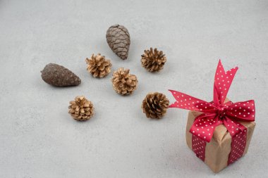 Kırmızı fiyonklu küçük bir hediye kutusu ve beyaz arka planda bir sürü kozalak.