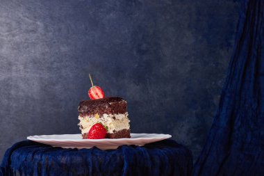 Mavi arka planda beyaz bir tabakta kakao ve çilekli bir dilim pasta. Yüksek kalite fotoğraf