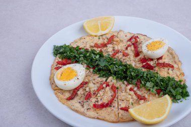 Biberli pizza, haşlanmış yumurta, limon ve yeşiller beyaz arka planda.